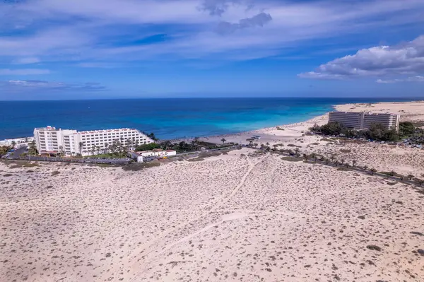 Corralejo, Fuerteventura 'da bir sahil otelinin görüntüsü. Görüntü, binaların canlı renklerini, kurak manzarayı ve hareketli tepeleri sergiliyor. Seyahat, gayrimenkul ve yaşam tarzı fotoğrafçılığı için mükemmel.. 