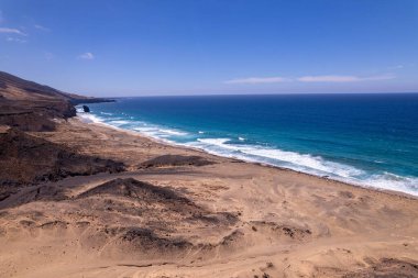 Fuerteventura 'daki Playa de Coffee' de Roque del Moro yakınlarındaki çarpıcı sahil kayalıklarını gösteren muhteşem hava görüntüleri. Görüntü kurak manzaranın, turkuaz suların ve uzak dağların, seyahat fotoğrafçılığının katıksız güzelliğini gözler önüne seriyor.. 