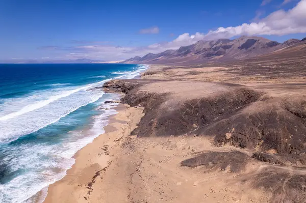 Fuerteventura 'daki Playa de Cofete' de Roque del Moro yakınlarındaki dramatik uçurum ve turkuaz suları görüntüleyen muhteşem hava görüntüleri. Görüntü, kırmızı toprağın, dağınık bitki örtüsünün ve uzak zirvelerin, seyahat fotoğrafçılığının katıksız güzelliğini gösteriyor.. 