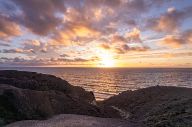 Fuerteventura 'daki La Pared yakınlarındaki kıyı kayalıklarında nefes kesen gün batımını çeken muhteşem hava görüntüleri. Görüntü gökyüzünün canlı renklerini, turkuvaz sularını ve seyahat fotoğrafçılığı için mükemmel engebeli araziyi sergiliyor.. 