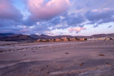 Fuerteventura 'daki büyüleyici bir köyde nefes kesen gün batımını çeken muhteşem hava görüntüleri. Görüntü gökyüzünün canlı renklerini, modern mimariyi ve kurak araziyi sergiliyor, seyahat ve yaşam tarzı fotoğrafçılığı için mükemmel..