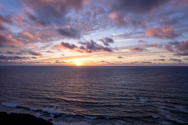 Fuerteventura 'daki La Pared yakınlarındaki kayalık uçurumlarda nefes kesen gün batımını çeken muhteşem hava görüntüleri. Görüntü gökyüzünün canlı renklerini, turkuvaz sularını ve seyahat fotoğrafçılığı için mükemmel engebeli araziyi sergiliyor.. 