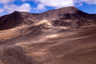Dinamik hava görüntüleri, Fuerteventura Jandia 'daki uzak dağlara giden dolambaçlı bir yolu gösteriyor. Görüntü, kırmızı toprağın, dağınık bitki örtüsünün ve seyahat ve macera fotoğrafçılığı için ideal uzak tepelerin saf güzelliğini yakalar..