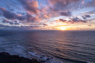 Kayalık kayalıkların ve Kanarya Adaları yakınlarındaki okyanus dalgalarının üzerindeki ılık günbatımı tonları. 