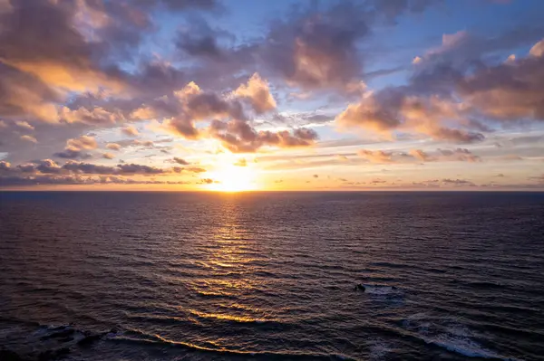 Detaylı hava görüntüleri Fuerteventura 'daki La Pared yakınlarındaki yuvarlanan tepelerin üzerinde gün batımını gösteriyor. Görüntü, yapılandırılmış yol ile engebeli arazi arasındaki zıtlığı vurguluyor ve bu da onu seyahat ve yaşam tarzı içeriği için ideal hale getiriyor.. 