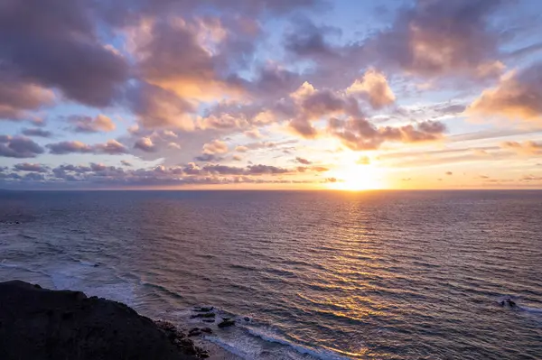 Fuerteventura 'daki La Pared' in uzak dağlarının yakınlarındaki çarpıcı günbatımını gösteren muhteşem hava görüntüleri. Görüntü kırmızı toprağın katıksız güzelliğini sergiliyor, dağınık bitki örtüsü, ve uzak tepeler, seyahat fotoğrafçılığı için mükemmel.. 