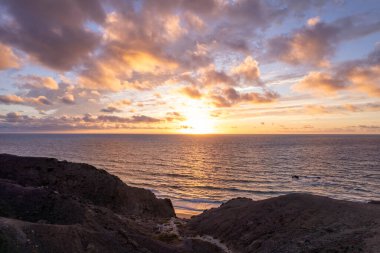 Dinamik hava çekimi Fuerteventura 'daki La Pared plajında çarpıcı günbatımını gösteriyor. Görüntü, altın kumlar, turkuaz sular ve engebeli arazi, seyahat, emlak ve yaşam tarzı fotoğrafçılığı arasındaki zıtlığı yakalıyor..