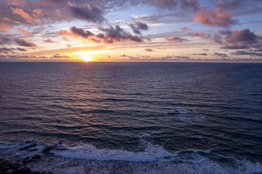 İspanya, Fuerteventura 'daki volkanik kayalıkların parlak günbatımı renkleri ve okyanus dalgaları. 