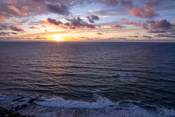 İspanya, Fuerteventura 'daki volkanik kayalıkların parlak günbatımı renkleri ve okyanus dalgaları. 