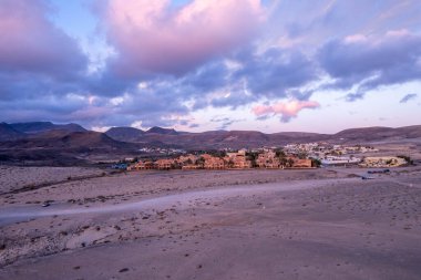 Dinamik hava görüntüleri Fuerteventura 'da gün batımında çarpıcı köyü gösteriyor. Görüntü, modern binalar ve engebeli arazi arasındaki zıtlığı, seyahat, emlak ve yaşam tarzı fotoğrafçılığı için ideal olanı yakalıyor.. 