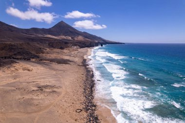 Detaylı hava görüntüleri Fuerteventura 'daki Playa de Cofete' de Roque del Moro yakınlarındaki dolambaçlı bir kıyı yolunu gösteriyor. Görüntü, yapılandırılmış yol ile engebeli arazi arasındaki kontrastı vurguluyor ve seyahat içeriği için ideal hale getiriyor. 