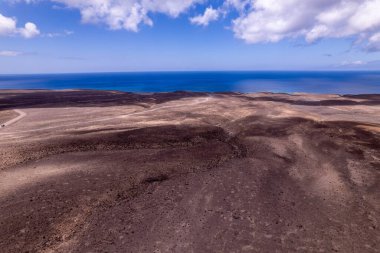 Detaylı hava görüntüleri Fuerteventura 'daki Jandia' nın turkuaz sularının yakınındaki dolambaçlı bir yolu gösteriyor. Görüntü, okyanusun yapılandırılmış yolu ile doğal güzelliği arasındaki zıtlığı vurguluyor. Bu da onu seyahat ve yaşam tarzı içeriği için ideal kılıyor.