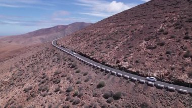 Fuerteventura 'da ufka uzanan düz bir yol yakalayan muhteşem hava görüntüleri. Görüntü, kırmızı toprağın, dağınık bitki örtüsünün ve uzak tepelerin, seyahat, doğa ve macera fotoğrafçılığı için mükemmel güzelliklerini sergiliyor.