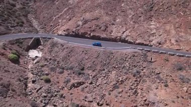 Fuerteventura 'daki dramatik kırmızı volkanik manzarayı kesen asfaltlı yolun geniş manzarası. Sahne, çorak güzelliği, derinliği ve seyahat potansiyelini yakalar..