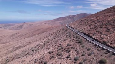 Fuerteventura 'daki görkemli dağların yakınındaki kıyı yolunu gösteren detaylı hava görüntüleri. Görüntü, turkuaz suların doğal güzelliği ile yapılandırılmış yol arasındaki zıtlığı vurguluyor. Bu da onu seyahat içeriği için ideal kılıyor.. 