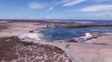 Dinamik hava çekimi Fuerteventura 'daki Playa El Majanicho yakınlarında dönen bir kıyı yolunu gösteriyor. Görüntü, yapılandırılmış yol ile engebeli arazi arasındaki zıtlığı, seyahat, emlak ve yaşam tarzı fotoğrafçılığı için ideal olanı yakalıyor.. 