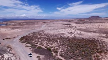 Fuerteventura 'daki Playa El Majanicho sahilinin yakınındaki büyüleyici köyü gösteren detaylı hava görüntüleri. Görüntü, kırmızı toprağın, dağınık bitki örtüsünün ve uzak tepelerin katıksız güzelliğini vurguluyor. Bu da onu macera içeriği için ideal kılıyor.. 