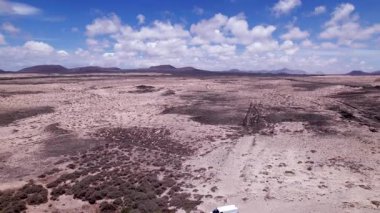 Detaylı hava görüntüleri Fuerteventura 'daki Playa El Majanicho sahilinin yakınındaki kurak araziyi gösteriyor. Görüntü, kırmızı toprağın, dağınık bitki örtüsünün ve uzak tepelerin katıksız güzelliğini vurguluyor. Bu da onu macera içeriği için ideal kılıyor.. 