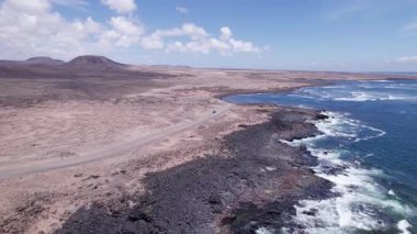 Dinamik hava çekimi Fuerteventura 'daki kayalık sahil boyunca dolambaçlı bir yol gösteriyor. Görüntü, yapılandırılmış yol ile engebeli arazi arasındaki zıtlığı, seyahat, emlak ve yaşam tarzı fotoğrafçılığı için ideal olanı yakalıyor.. 