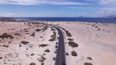 Fuerteventura 'daki sahil kasabasının yakınındaki virajlı bir yolu yakalayan muhteşem hava görüntüleri. Görüntü, kırmızı toprağın, dağınık bitki örtüsünün ve uzak tepelerin katıksız güzelliğini sergiliyor. Seyahat, gayrimenkul ve yaşam tarzı fotoğrafçılığı için mükemmel.. 