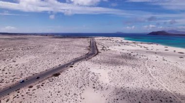 Detaylı hava görüntüleri, Fuerteventura, Corralejo 'daki kurak araziyi kesen dolambaçlı bir yolu gösteriyor. Görüntü, kırmızı toprağın, dağınık bitki örtüsünün ve uzak tepelerin katıksız güzelliğini vurguluyor. Bu da onu seyahat içeriği için ideal kılıyor..