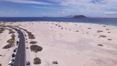 Fuerteventura 'daki deniz paraşütü noktasının yakınındaki virajlı bir yolu kaydeden muhteşem hava görüntüleri. Görüntü, kırmızı toprağın, dağınık bitki örtüsünün ve uzak tepelerin katıksız güzelliğini sergiliyor. Seyahat, gayrimenkul ve yaşam tarzı fotoğrafçılığı için mükemmel..