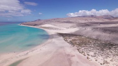 Dinamik hava görüntüleri Fuerteventura 'daki Costa Calma dağlarının yakınındaki çarpıcı kıyı manzarasını gösteriyor. Görüntü, yapılandırılmış yol ile engebeli arazi arasındaki zıtlığı, seyahat, emlak ve yaşam tarzı fotoğrafçılığı için ideal olanı yakalıyor..