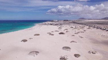 Dinamik hava görüntüleri, Fuerteventura, Corralejo 'daki okyanus yakınlarındaki çarpıcı çöl manzarasını gösteriyor. Görüntü, yapılandırılmış yol ile engebeli arazi arasındaki zıtlığı, seyahat, emlak ve yaşam tarzı fotoğrafçılığı için ideal olanı yakalıyor.. 