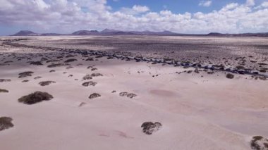 Fuerteventura, Corralejo 'daki çölün yakınlarında dönen bir kıyı yolunu görüntüleyen muhteşem hava görüntüleri. Görüntü kırmızı toprağın katıksız güzelliğini, dağınık bitki örtüsünü ve uzak tepeleri gösteriyor. Seyahat ve yaşam tarzı fotoğrafçılığı için mükemmel..