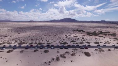 Corralejo, Fuerteventura 'daki kayalık sahil boyunca uzanan virajlı bir yolu yakalayan muhteşem hava görüntüleri. Görüntü kırmızı toprağın katıksız güzelliğini, dağınık bitki örtüsünü ve uzak tepeleri gösteriyor. Seyahat ve yaşam tarzı fotoğrafçılığı için mükemmel..