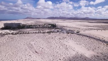 Detaylı hava görüntüleri Fuerteventura 'daki çarpıcı kıyı manzarasını modern binalarla yakalıyor. Görüntü, kırmızı toprağın, dağınık bitki örtüsünün ve uzak tepelerin katıksız güzelliğini vurgular. Bu da onu seyahat için ideal kılar, doğa içeriği.. 