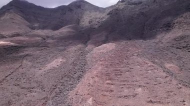 Kahveye, Fuerteventura 'daki dağların yakınındaki kurak araziyi gösteren muhteşem hava görüntüleri. Görüntü kırmızı toprağın katıksız güzelliğini, dağınık bitki örtüsünü ve uzak tepeleri sergiliyor. Yolculuk için mükemmel, doğa fotoğrafçılığı..
