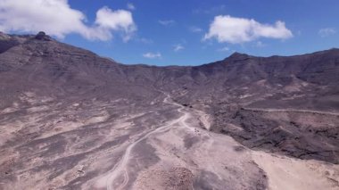 Fuerteventura 'daki dramatik kırmızı volkanik manzarayı kesen asfaltlı yolun geniş manzarası. Sahne, çorak güzelliği, derinliği ve seyahat potansiyelini yakalar..