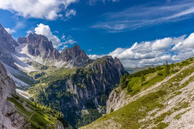 Dolomiti Alpleri güzel dağ manzarası. Dolomitlerde Rocky kulesi zirveleri. Yeşil dağ vadisindeki yürüyüş yolunda yaz manzarası ve bulutlu mavi gökyüzü.