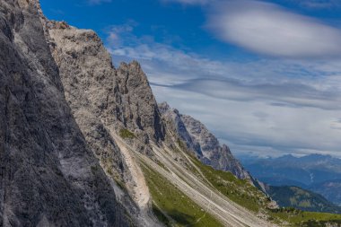 Dolomiti Alpleri güzel dağ manzarası. Dolomitlerde Rocky kulesi zirveleri. Yeşil dağ vadisindeki yürüyüş yolunda yaz manzarası ve bulutlu mavi gökyüzü.