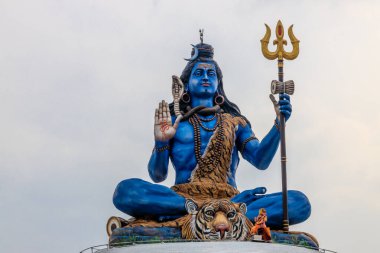 Lord Shiva 'nın mavi heykeli kaplan derisinden yapılmış, mızrak tutuyor ve kutsal bir jest sergiliyor. Yılanlar ve boncuklarla süslenmiş bu canlı heykel, berrak bir gökyüzüne karşı görkemli bir şekilde duruyor.