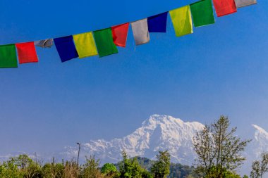 Nepal 'in görkemli dağlarında dalgalanan renkli Nepal ve Tibet dua bayrakları. Barışı, merhameti ve bereketi simgeleyen bayraklar Himalaya dağlarının sakin manzarasını süslüyor.