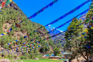 Nepal 'in görkemli dağlarında dalgalanan renkli Nepal ve Tibet dua bayrakları. Barışı, merhameti ve bereketi simgeleyen bayraklar Himalaya dağlarının sakin manzarasını süslüyor.