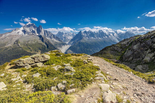Tour du Montblanc beautiful mountain ladscapes of the Alps green valley, snow summit of Montblanc and rocky peaks of Aiguille du Midi in summer sunny weather blue sky, trekking and hiking in Chamonix