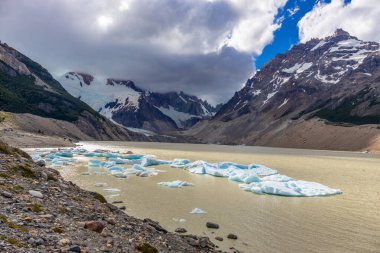 El Chalten, Arjantin 'deki Patagonya dağları. Monte Fitzroy ve Cerro Torre göl kıyısındaki granit duvarlara tırmanıyor. Buz dağları yüzen buzdağları ve kara bulutlarla. Patagonya havası ve dağ sıraları.