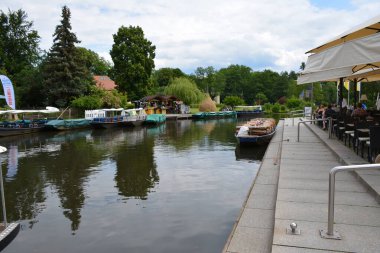 Bu büyüleyici görüntü, Almanya 'nın pitoresk bir bölgesi olan Lubbenau / Spreewald' ın dingin güzelliğini yansıtıyor. Fotoğrafta yemyeşil sularda salınan sakin bir kanal var. Geleneksel tekneler suyun üzerinde nazikçe yüzüyor. Yoğun orman