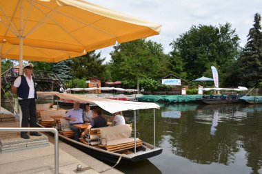 Bu büyüleyici görüntü, Almanya 'nın pitoresk bir bölgesi olan Lubbenau / Spreewald' ın dingin güzelliğini yansıtıyor. Fotoğrafta yemyeşil sularda salınan sakin bir kanal var. Geleneksel tekneler suyun üzerinde nazikçe yüzüyor. Yoğun orman