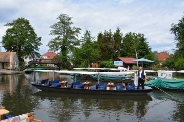 Bu büyüleyici görüntü, Almanya 'nın pitoresk bir bölgesi olan Lubbenau / Spreewald' ın dingin güzelliğini yansıtıyor. Fotoğrafta yemyeşil sularda salınan sakin bir kanal var. Geleneksel tekneler suyun üzerinde nazikçe yüzüyor. Yoğun orman