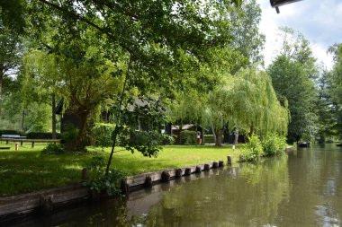 Bu büyüleyici görüntü, Almanya 'nın pitoresk bir bölgesi olan Lubbenau / Spreewald' ın dingin güzelliğini yansıtıyor. Fotoğrafta yemyeşil sularda salınan sakin bir kanal var. Geleneksel tekneler suyun üzerinde nazikçe yüzüyor. Yoğun orman