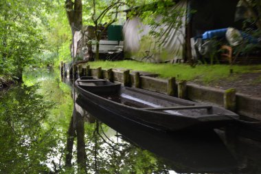Bu büyüleyici görüntü, Almanya 'nın pitoresk bir bölgesi olan Lubbenau / Spreewald' ın dingin güzelliğini yansıtıyor. Fotoğrafta yemyeşil sularda salınan sakin bir kanal var. Geleneksel tekneler suyun üzerinde nazikçe yüzüyor. Yoğun orman