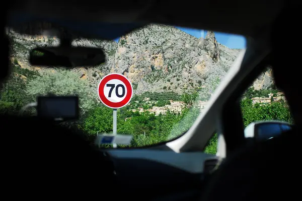 Araba içinde çekilmiş bir fotoğraf bir yolculuk sırasında manzaralı bir dağ yolunda 70 hız limiti işareti gösteriyor. Alpes-de-Haute-Provence, Le Sauze du Lac, Fransa Turu