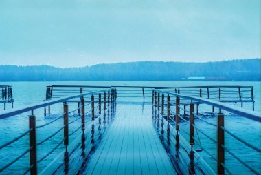 Sis kaplı dağlarla çevrili, sisli bir göle uzanan sakin bir rıhtım, sakin bir manzara yaratır.