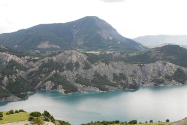 Sakin bir göl boyunca uzanan dolambaçlı dağ yolu doğal manzaranın nefes kesici manzarasını sunuyor. Hız göstergesi, Alpes-de-Haute-Provence, Tour de France, Le Sauze du Lac