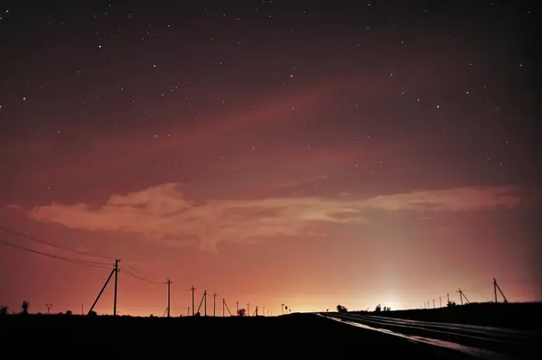 Parlak yıldızlı huzurlu bir gece manzarası, alacakaranlık bulutları, ve sakin bir gökyüzüne karşı siluetli elektrik hatları