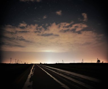 Bulutlu bir gökyüzünün altında dolambaçlı bir yolun yer aldığı sakin bir gece sahnesi..